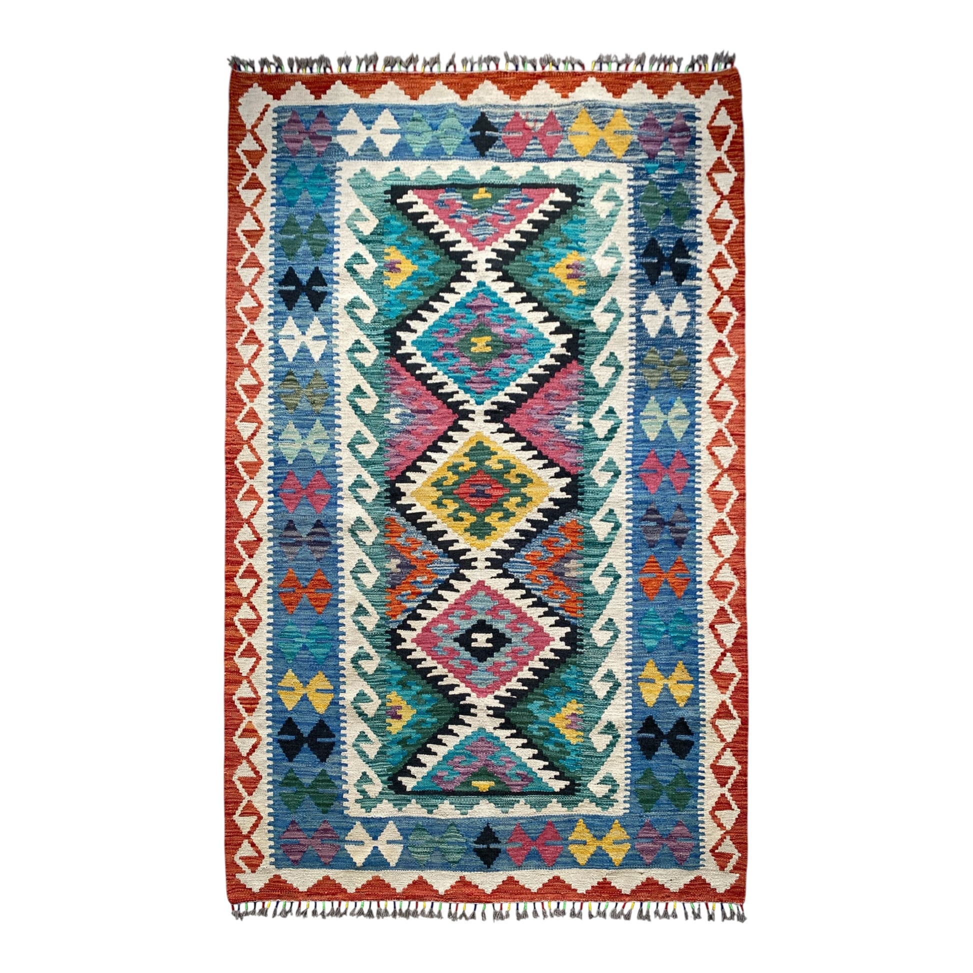 A hand woven area kelim rug with a vibrant Turkish Nomadic geometric pattern, featuring a central diamond motif in pink, yellow, blue, and black on a cream background, surrounded by a red and blue border with fringe on the top and bottom.